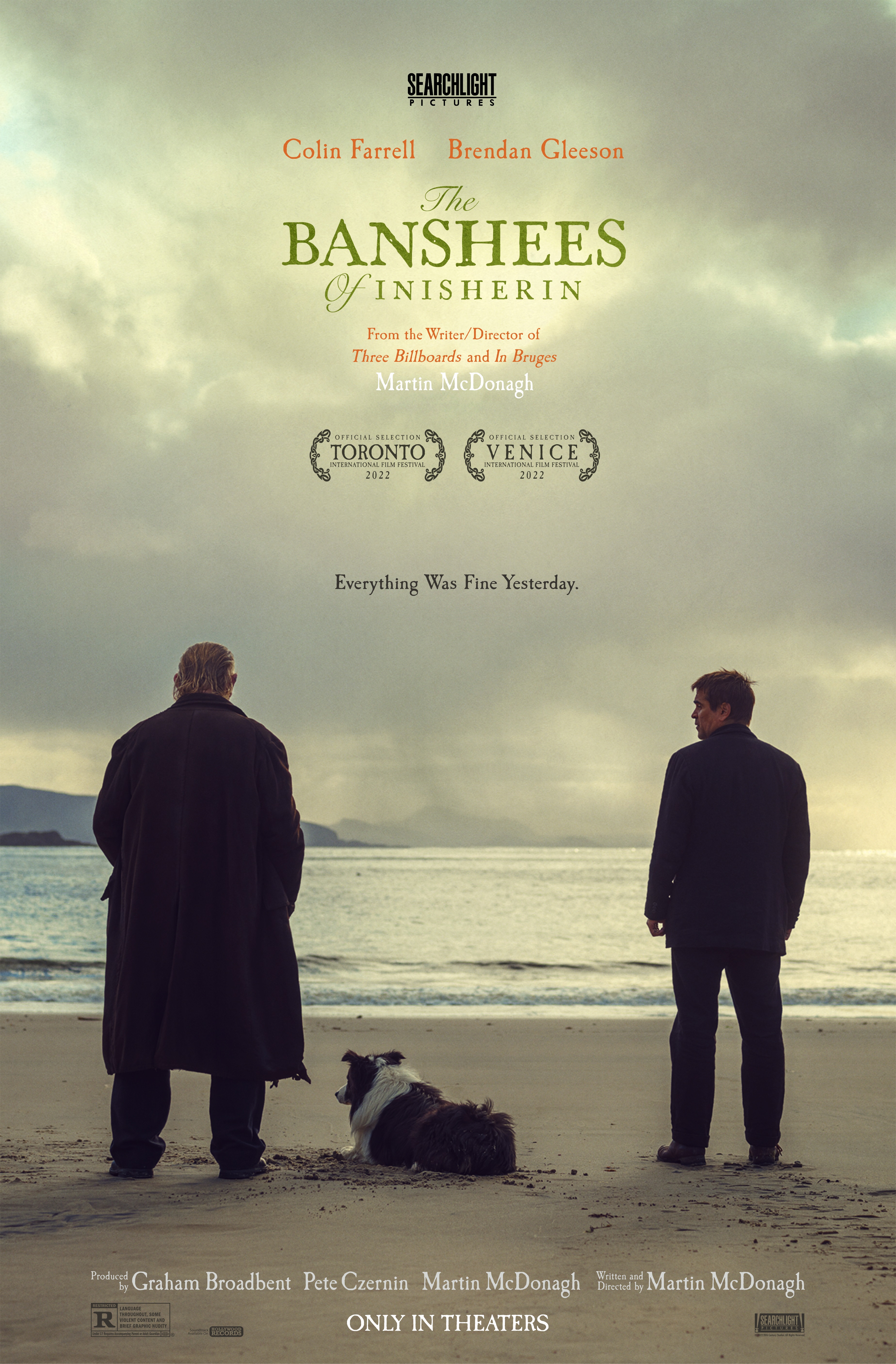 Two men standing on the beach with a dog laying down in-between them.