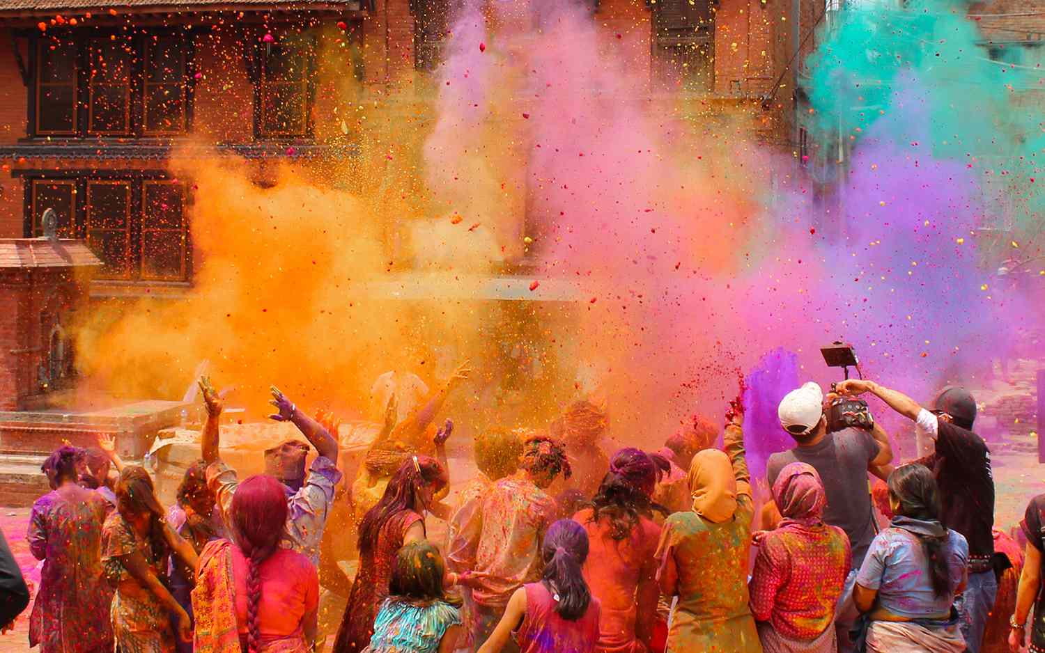 a crowd of people in India throwing colored powder in the air in celebration