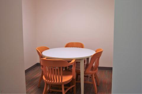 A small room with a round, white table and four orange chairs in the center.