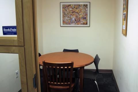 A view of a small room through its door. A small, round, wooden table with 4 chairs is located in the center of the room.