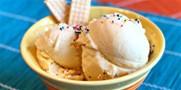 Two scoops of ice-cream are nestled into a white dessert bowl, lightly dusted with multi-colored sugar sprinkles, with two vanilla wafers tucked into one side of the bowl.