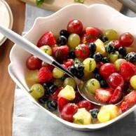 A medley of various fruits topped with mint ambrosia are in a scalloped edge ceramic bowl with a spoon.