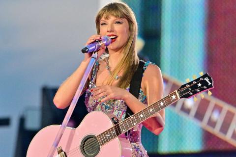 Photo of Taylor Swift holding a pink guitar and speaking into a microphone