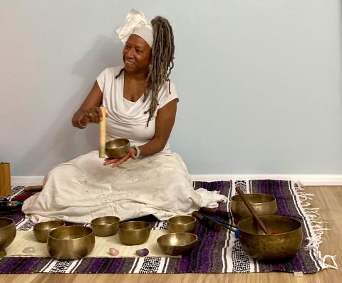 A woman sitting with singing bowls and a light blue background.