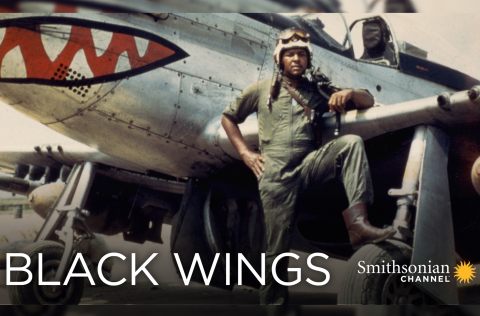 African American man standing against a silver fighter plane.