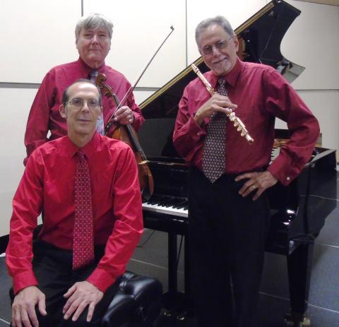 Three men wearing red shirts posing in front of a piano with their instruments.