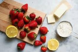 Lemons, and strawberries are tantalizingly sprawled against a marble countertop along with cream and a stick of butter.