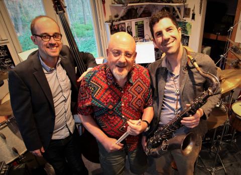 Three men smiling.  One is wearing red, another is wearing plaid and another one wearing a black jacket.