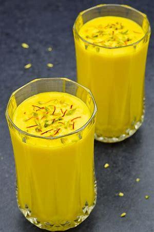 2 clear glasses filled with mango lassi topped with saffron, cardamon and pistachio