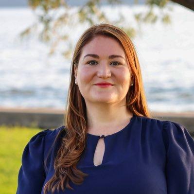 Woman wearing blue with blue water and green grass in the background.