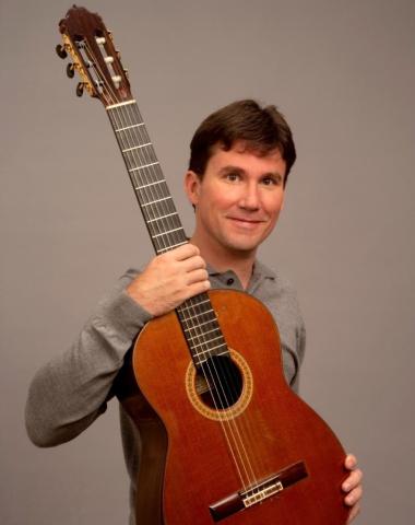 Guitarist Peter Fletcher holding his guitar with a gray background.