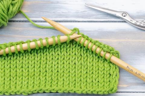 Knitting materials, knitting green yarn and two tan needles and gray background.