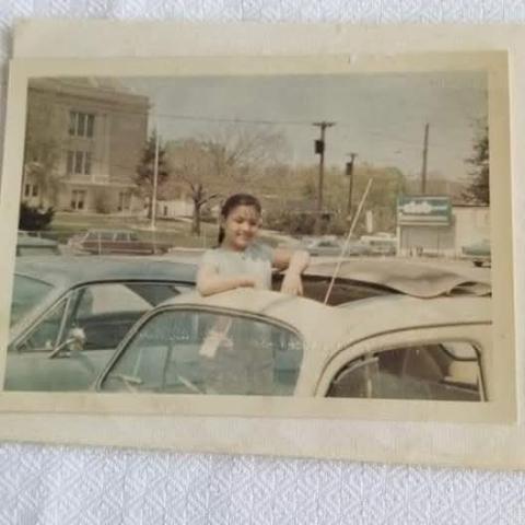 Little girl standing up in a convertible with blue sky and trees in the background.