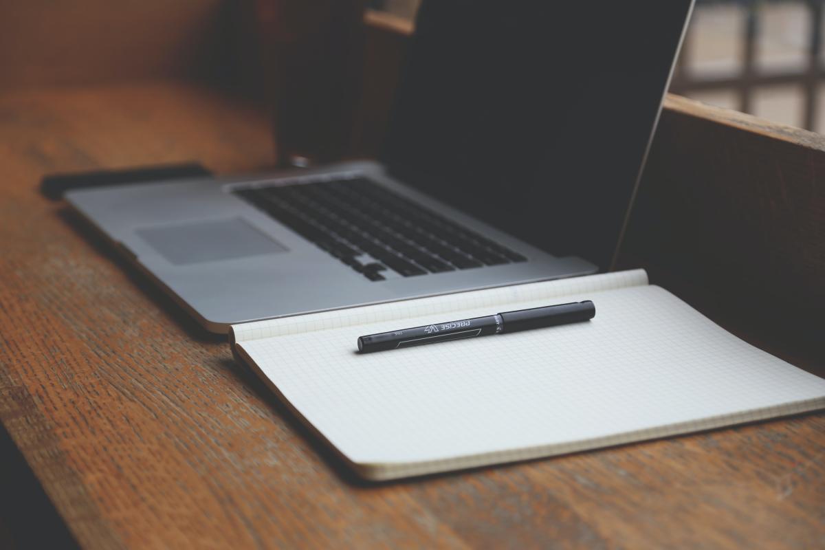 Laptop open next to a paper notebook