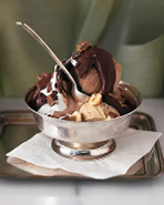 A silverware dessert bowl holds almonds nestled within heaping mounds of rocky road ice cream, and drizzled with chocolate sauce,