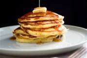 Haphazardly stacked silver dollar pancakes sit atop a ice-blue plate, liberally drizzled with butter and syrup.