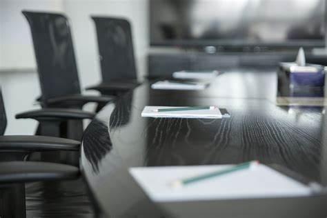 Partial view of a table with chairs around it. Paper and pen on the table.