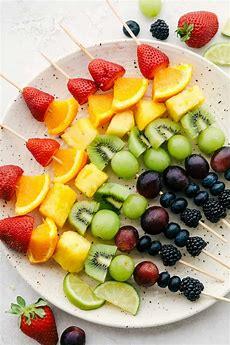 a plate of kabobs made with strawberries, oranges, pineapple, kiwi, and grapes