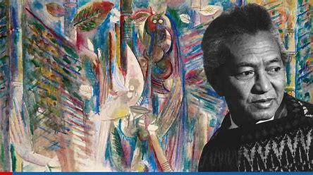 a photograph of Wilfredo Lam in front of a piece of his multicolored artwork