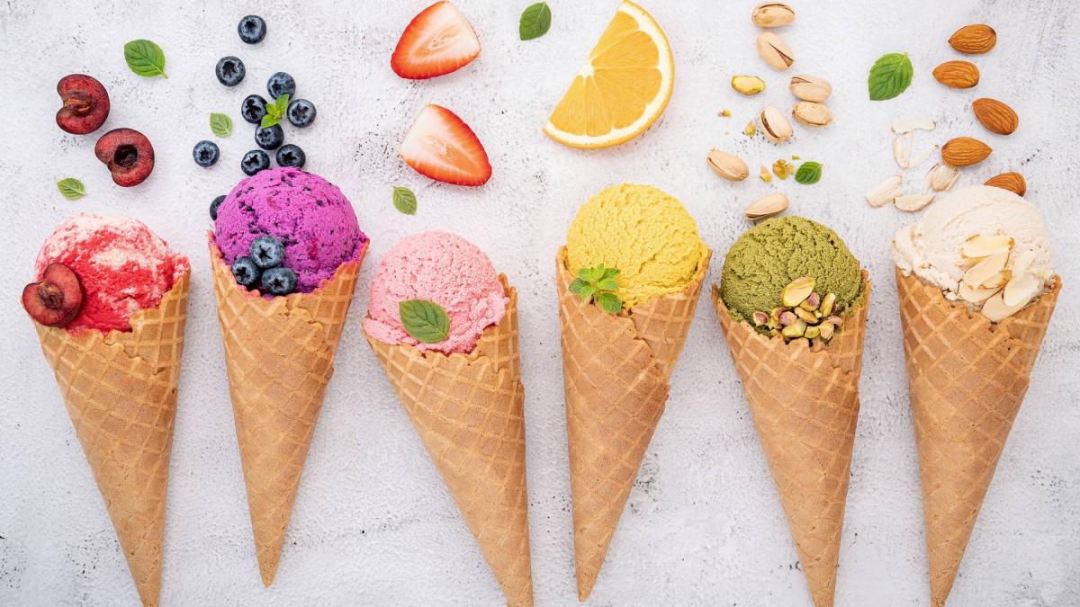 Six cones with different color gelatos in them on a white background.