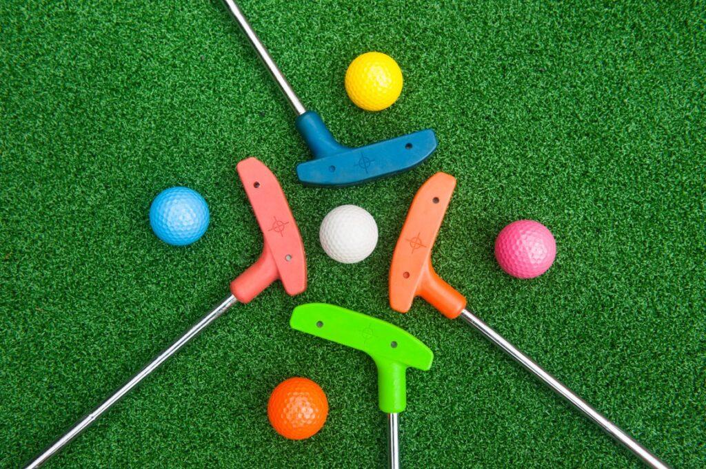 Green, orange, red, blue mini golf clubs and golf balls.