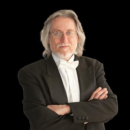 Man in gray hair and a black tuxedo with a black background.