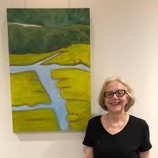 Artist in black shirt standing in front of light & dark green with blue painting.