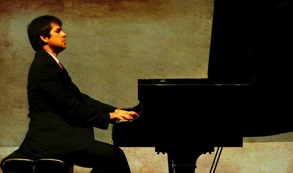 Pianist Itay Goren playing piano with a greenish background.