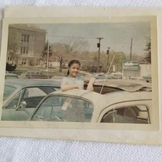 Little girl standing up in a convertible with blue sky and trees in the background.